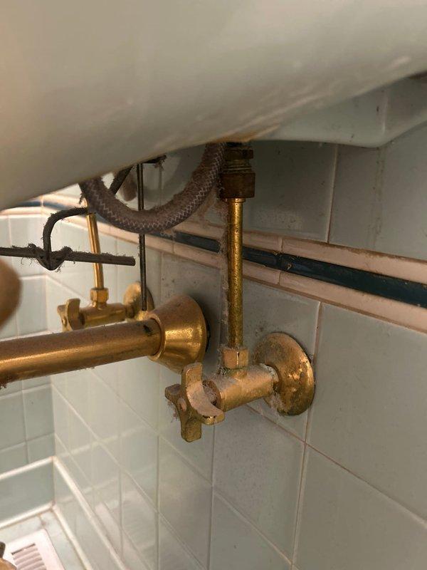 Conducted comprehensive plumbing assessment for pedestal sink replacement and leaking bathtub faucet repair. Inspected existing copper supply lines, brass shut-off valves, and flexible braided connections under current sink installation, noting age-related tarnishing and minor corrosion on valve components. Evaluated bathroom fixture configuration including white pedestal sink with brushed nickel faucet assembly and surrounding tile work to provide accurate estimate for replacement and repair services.