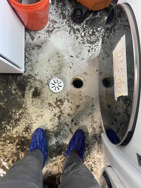 Responded to emergency call for flooded basement following heavy rainfall. Upon arrival, found extensive water damage throughout utility room with standing water covering concrete floor, visible sediment, debris, and significant moisture infiltration affecting multiple drain points. Assessed three floor drains in mechanical space, one equipped with plastic grate and two uncovered openings showing signs of backup or overflow. Deployed water extraction equipment and protective measures, including tarping of vulnerable mechanical equipment to prevent further damage to HVAC systems and appliances. Documented severe floor discoloration, mold growth patterns, and biological contamination resulting from water intrusion. Identified compromised drainage system as primary cause of flooding, with floor drains unable to handle volume of water entering space. Extracted standing water from affected areas using commercial-grade vacuum equipment and assessed extent of water damage to surrounding surfa