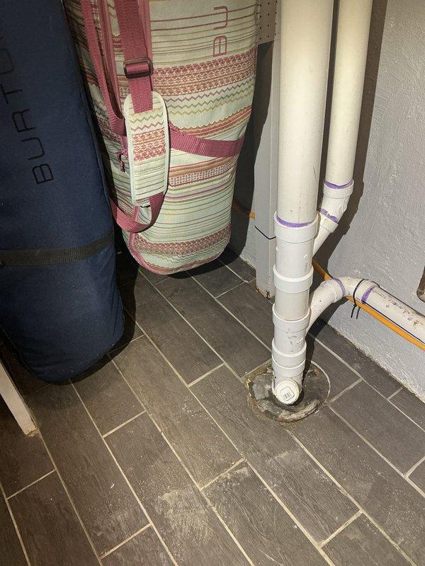 Conducted site evaluation for standpipe installation in 70-year-old residence experiencing recurring basement flooding issues. Assessed existing floor drain with significant sediment buildup and standing water, documented drainage infrastructure condition, and evaluated two PVC pipe penetrations in tiled floor area to determine optimal standpipe placement and drainage solution for flood prevention.