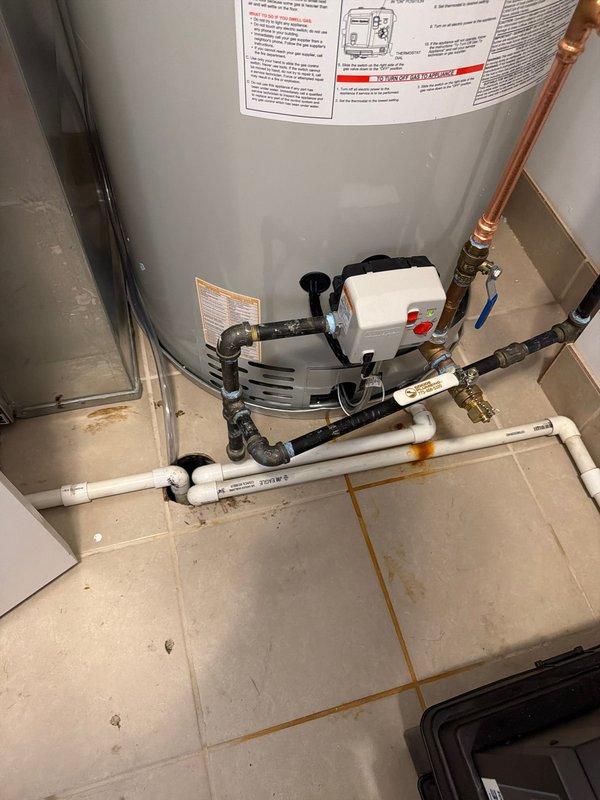 Completed same-day gold-level water heater installation in residential utility space. Installed new Bradford White tanked water heater with complete plumbing connections including copper supply lines, blue-handled isolation valve, expansion tank mounted to wall, and black circulation pump on top of unit. Connected PVC drainage piping at floor level and integrated white plastic manifold distribution system with multiple valve connections. All connections properly secured with appropriate fittings and joints, system tested and operational.