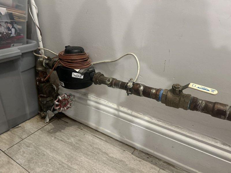 Responded to service call to provide estimate for emergency main water shut-off valve replacement located before the meter. Upon inspection, found existing shut-off valve exhibiting severe corrosion, rust buildup along brazed seams, and green copper oxidation indicating advanced deterioration and potential failure risk. Documented existing plumbing configuration including red-handled gate valve, white-handled ball valve, and associated piping assembly for estimate preparation.