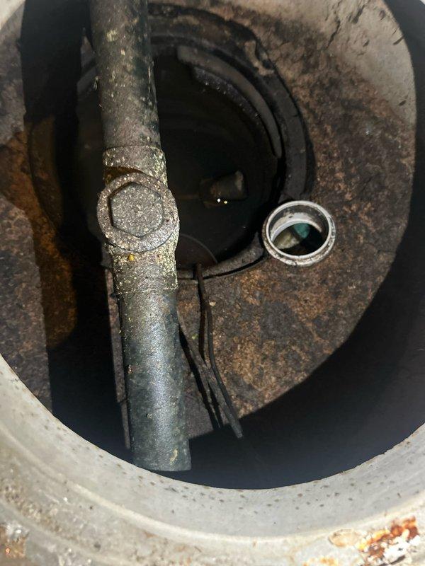 # Sump Pump Failure Assessment and Repair

Responded to service call for non-functioning sump pump system. Upon arrival, conducted thorough inspection of sump pit and pump assembly. Found severely corroded discharge pipe with extensive rust and mineral buildup throughout the piping system, compromising structural integrity and flow capacity. Standing water present in basin indicated pump failure to activate or discharge properly.

Documented existing conditions showing deteriorated metal piping with grayish-green patina and brownish corrosion, concrete basin with rust staining and age-related degradation, and sensor/float components at pit bottom. Identified black wiring running along pit floor connected to pump controls.

Removed failed sump pump unit and assessed discharge line condition. Due to advanced corrosion state of existing metal piping, recommended and performed complete replacement of discharge assembly. Installed new discharge piping to ensure proper water evacuation and p