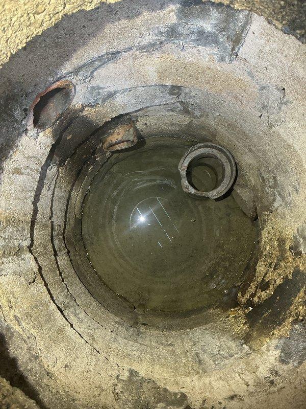 Responded to service call for flood control system inspection and functionality check. Upon arrival, conducted thorough assessment of the flood control infrastructure, including exterior drainage access point and surrounding areas. Inspected cylindrical concrete drainage structure and found standing water with visible sediment accumulation and algae growth at the bottom. Observed weathered concrete surfaces with age-related cracking and staining throughout the structure. Verified structural integrity of concrete walls and metal fittings, noting corrosion on embedded metal ring component consistent with environmental exposure. Examined exterior patio area adjacent to flood control system, documenting heavily stained concrete surfaces showing signs of moisture-related discoloration and organic buildup. Assessed drainage patterns and water flow pathways to ensure proper functionality of the flood control system. Confirmed all mechanical components and drainage infrastructure were operatio