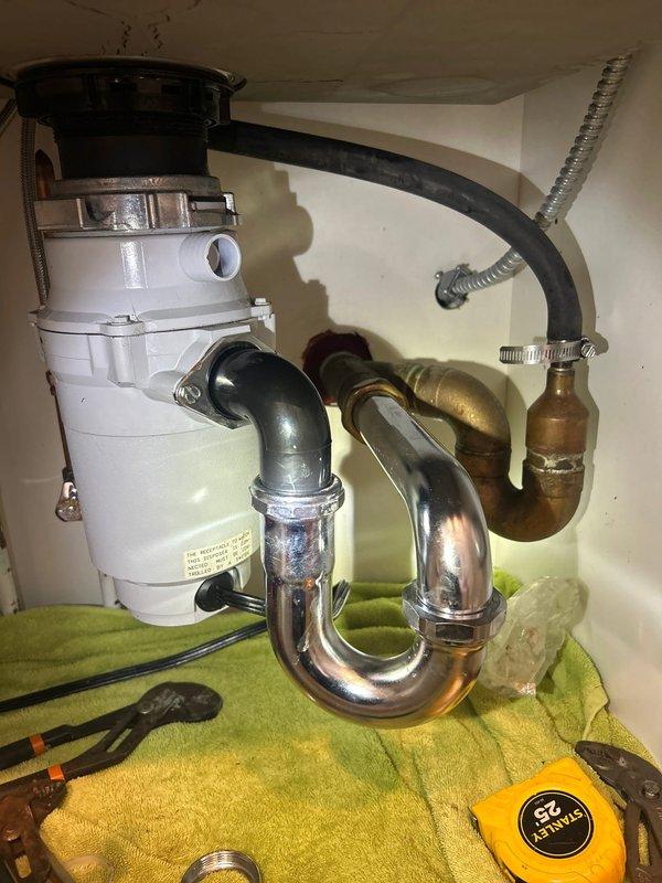 Responded to service call for kitchen sink leak underneath cabinet. Upon inspection, identified leak originating from garbage disposal connections and P-trap assembly. Disassembled and inspected disposal mounting flange, drain connections, and trap piping. Replaced worn gaskets and seals at disposal discharge connection. Tightened all slip-joint connections on chrome P-trap assembly and verified proper alignment of drain piping. Tested system by running water through sink and operating garbage disposal unit to confirm leak was resolved and all connections were secure with no further dripping.