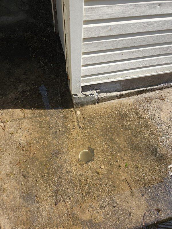 Responded to a residential drainage issue where a sidewalk drain cover had come off and the drain basin was completely filled with dirt and debris. Accessed the property through the rear alley to assess the ground-level drain located along the side walkway near the building exterior. Documented the condition of the concrete pad showing weathering, the exposed drain opening, and surrounding deterioration requiring cleanout and potential drain cover replacement to restore proper drainage function.