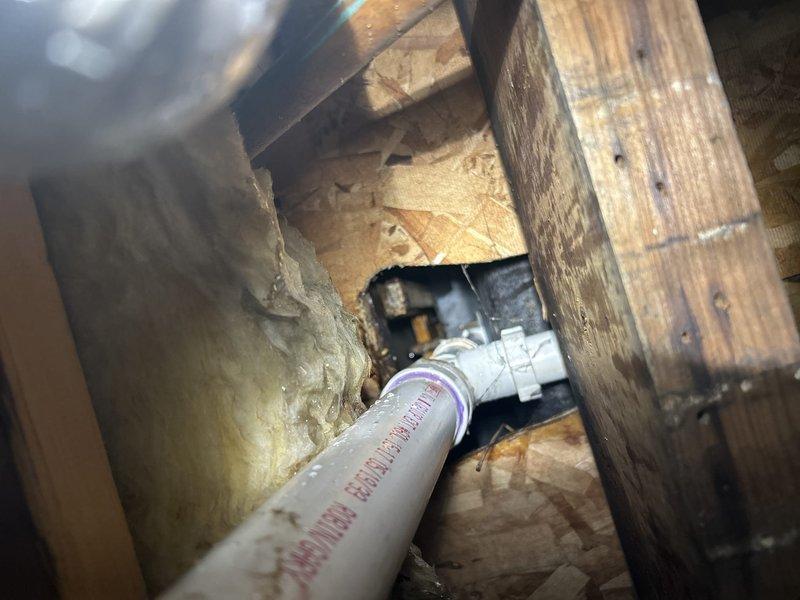 Responded to water leak originating from bathroom exhaust fan area on lower level, with source traced to plumbing system in unit above. Accessed ceiling cavity and inspected PVC drain trap and surrounding structural components, identifying water staining on wooden framing members and confirming leak location from upper bathroom plumbing. Documented conditions with photographs showing exposed drain line configuration, insulation, and evidence of water intrusion for further repair coordination.