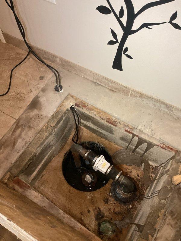 Responded to emergency basement flooding caused by sump pump system failure. Upon arrival, found clear water backing up through utility sink and sump pit, with flood control system unable to keep pace with incoming water. Inspected sump pump assembly and discovered pump malfunction preventing proper discharge of groundwater accumulation. Removed debris and sediment from sump pit that had accumulated around pump intake, affecting operational efficiency. Examined cast iron drainage piping and ejector pump connections beneath utility sink, identifying compromised drainage pathway contributing to backup condition. Cleared obstruction in drainage line allowing water to flow freely through system. Tested sump pump operation after cleaning and verified proper cycling and discharge function. Confirmed flood control system returned to normal operation with water level stabilizing in sump pit. Advised on visible deterioration of wooden framing around plumbing access area and recommended monitori