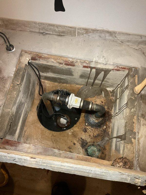 Responded to emergency basement flooding caused by sump pump system failure. Upon arrival, found clear water backing up through utility sink and sump pit, with flood control system unable to keep pace with incoming water. Inspected sump pump assembly and discovered pump malfunction preventing proper discharge of groundwater accumulation. Removed debris and sediment from sump pit that had accumulated around pump intake, affecting operational efficiency. Examined cast iron drainage piping and ejector pump connections beneath utility sink, identifying compromised drainage pathway contributing to backup condition. Cleared obstruction in drainage line allowing water to flow freely through system. Tested sump pump operation after cleaning and verified proper cycling and discharge function. Confirmed flood control system returned to normal operation with water level stabilizing in sump pit. Advised on visible deterioration of wooden framing around plumbing access area and recommended monitori