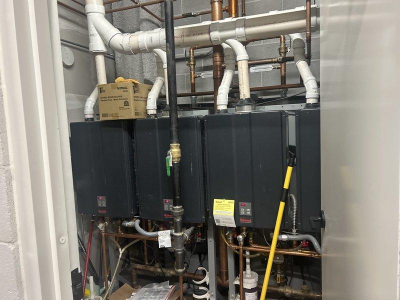 Completed plumbing estimate for dual tankless water heater installation with comprehensive piping assessment. Documented existing copper supply lines, brass valve configurations, PVC venting system, and pressure monitoring equipment. Photographed complete mechanical assembly including gas connections, exhaust routing, and control components for proposal development.
