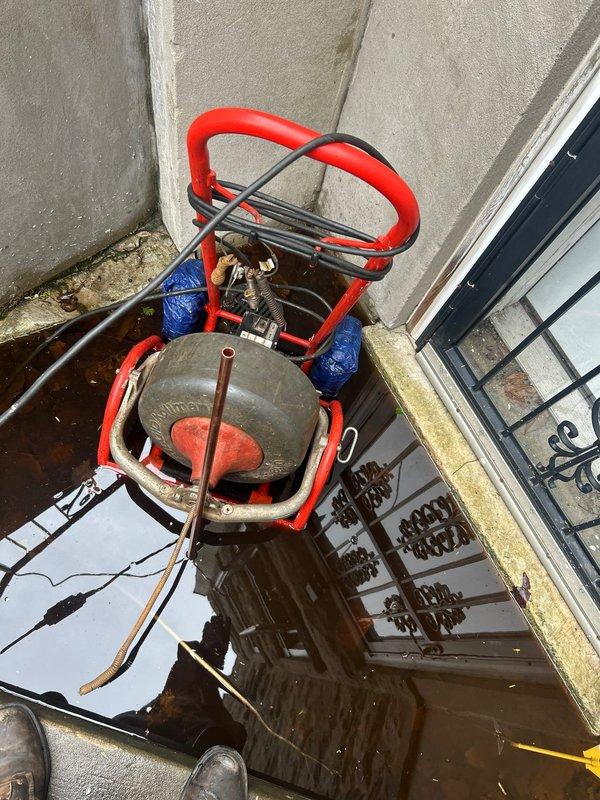 Responded to a clogged outdoor drain causing severe flooding in an exterior basement stairwell. Deployed rodding equipment to clear the blockage from the below-grade drain system, which had resulted in standing water completely submerging the lower stairwell area. Successfully cleared the obstruction and restored proper drainage function to the outdoor drain line.