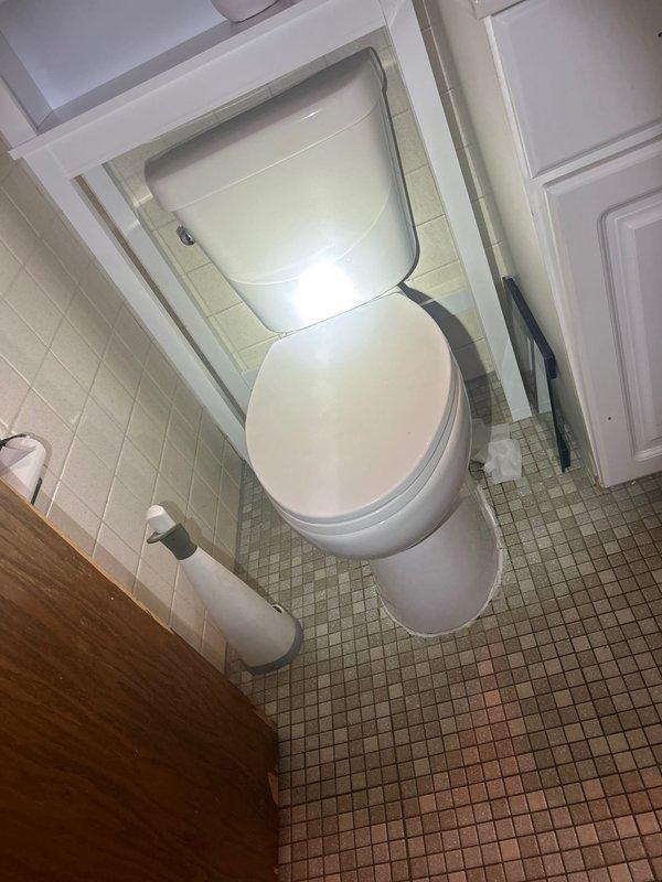 Responded to customer report of water leak behind toilet in residential bathroom. Conducted visual inspection of toilet installation, surrounding floor tiles, and wall connections. Documented existing conditions including mosaic tile flooring with visible water damage and discoloration, white subway tile walls, and standard two-piece toilet fixture. Assessed leak source and provided estimate for necessary piping repairs to address water infiltration issue.