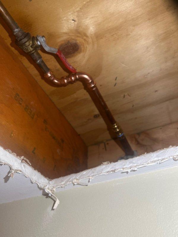 Responded to emergency call for water leak affecting basement ceiling when outdoor spigot was activated. Accessed plumbing through ceiling opening to locate source of leak in supply line serving exterior hose bib. Installed new ball valve with red handle and brass elbow fitting on copper supply line within ceiling cavity. Tested system for proper operation and verified no additional leaks present after repairs completed.