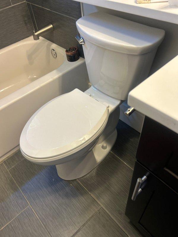 Completed installation of customer-supplied two-piece toilet in bathroom with gray wood-grain tile flooring. Removed existing toilet, prepared flange with new wax ring seal, positioned and secured new toilet unit, and verified proper water supply connection and operation. All fixtures installed according to manufacturer specifications with no leaks detected upon testing.