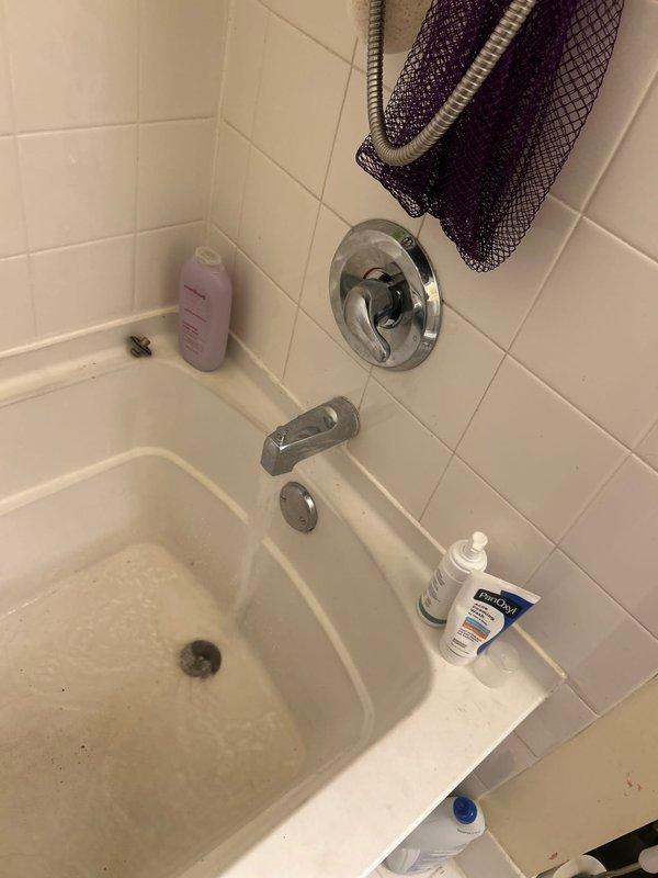 Completed installation of chrome bathtub fixtures in residential bathroom, including wall-mounted tub spout, shower control valve with circular escutcheon plate, and drain assembly. All fixtures were properly mounted to white tile walls and tested for proper operation and water flow.