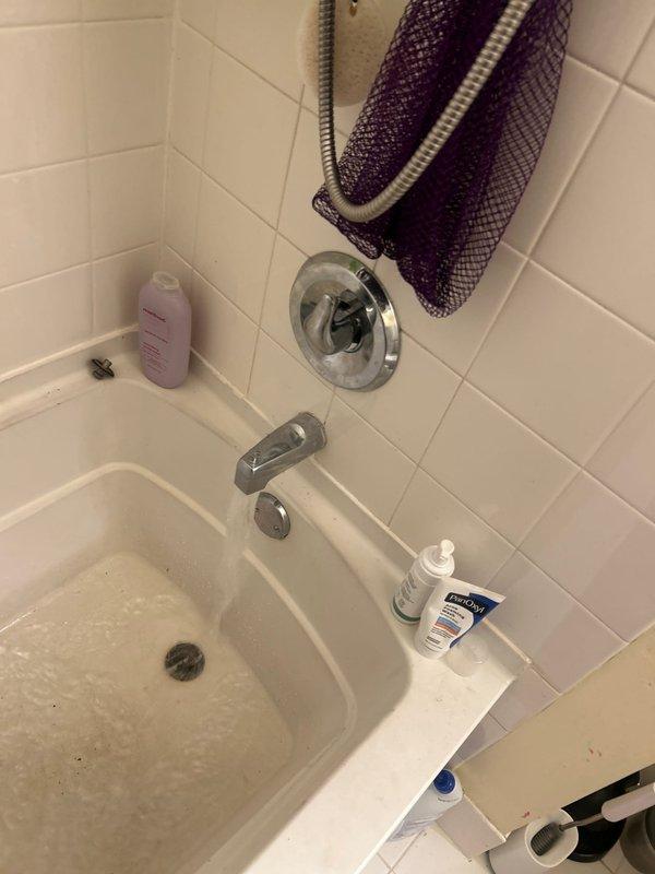 Completed installation of chrome bathtub fixtures in residential bathroom, including wall-mounted tub spout, shower control valve with circular escutcheon plate, and drain assembly. All fixtures were properly mounted to white tile walls and tested for proper operation and water flow.