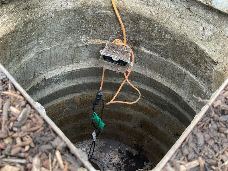 Responded to service call for non-functioning external flood prevention system at 60-year-old residential property. Upon inspection, discovered issues with underground sump pit and drainage well system located in yard near street. Accessed deep concrete cistern well with precast construction showing age-related weathering and moisture accumulation. Inspected suspended pump equipment and monitoring components via access rope system. Examined secondary concrete utility pit containing PVC drainage lines and plumbing connections with standing water present. Assessed pump operation, drainage flow patterns, and structural integrity of both underground containment systems. Documented conditions via photography for maintenance records. System had been inoperative for approximately two days prior to service call, requiring immediate attention to restore flood control functionality and prevent potential property damage.