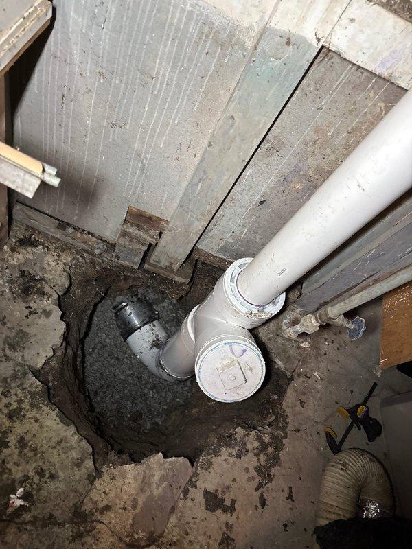 Conducted site assessment of basement plumbing infrastructure and identified deteriorated concrete flooring surrounding vertical PVC drain stack. Documented existing conditions including compromised floor area with accumulated sediment and moisture around pipe penetration point, exposed T-junction drainage configuration, and aging utility space requiring structural attention. Provided comprehensive photographic documentation of plumbing system layout and recommended repair solutions for concrete restoration and proper sealing around pipe installations to prevent future deterioration.