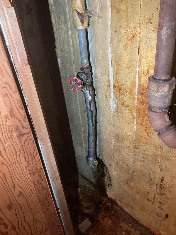 Conducted comprehensive drain and sewer assessment for commercial facility, focusing on under-sink plumbing infrastructure and main water supply systems. Documented existing P-trap configuration with white PVC piping, flexible supply lines, and pump assembly unit mounted beneath basin fixture, noting age-related discoloration on metal fittings and evidence of previous moisture exposure on surrounding wooden surfaces. Evaluated main water supply line with shutoff valve in utility area, identifying system conditions and photographing infrastructure for estimate preparation purposes.