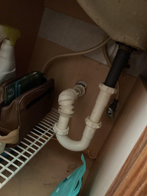 Responded to active water leak at bathroom sink drainage system in 110-year-old residential property. Upon inspection, identified leak source at junction where vertical and horizontal PVC drain pipes meet beneath sink, specifically at the P-trap connection point. Accessed plumbing through vanity cabinet and assessed compromised pipe joint assembly. Created ceiling access point to inspect vertical drain pipe routing through floor joists and verify extent of water damage to surrounding structural components. Documented existing white PVC P-trap configuration with elbow joint connections and vertical drain assembly. Photographed compromised plumbing connections and exposed ceiling cavity showing black drain pipe secured to wooden framing members. Completed four-hour service call addressing immediate leak concern and providing assessment of aging drainage infrastructure.