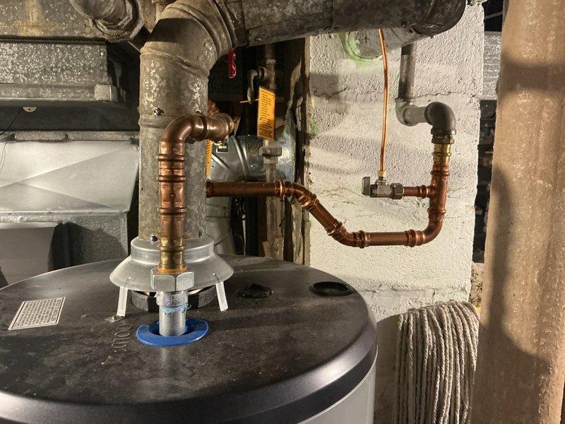 Conducted site assessment for water heater elevation and backflow prevention installation. Evaluated existing tanked water heater installation with copper piping connections and identified basement moisture concerns based on visible floor staining and presence of dehumidifier unit. Provided estimate for constructing elevated platform to raise water heater above potential flood level and installing backflow valve to protect potable water supply from contamination. Documented current plumbing configuration including copper supply lines, compression fittings, and wall-mounted connections to determine material and labor requirements for proposed upgrades.