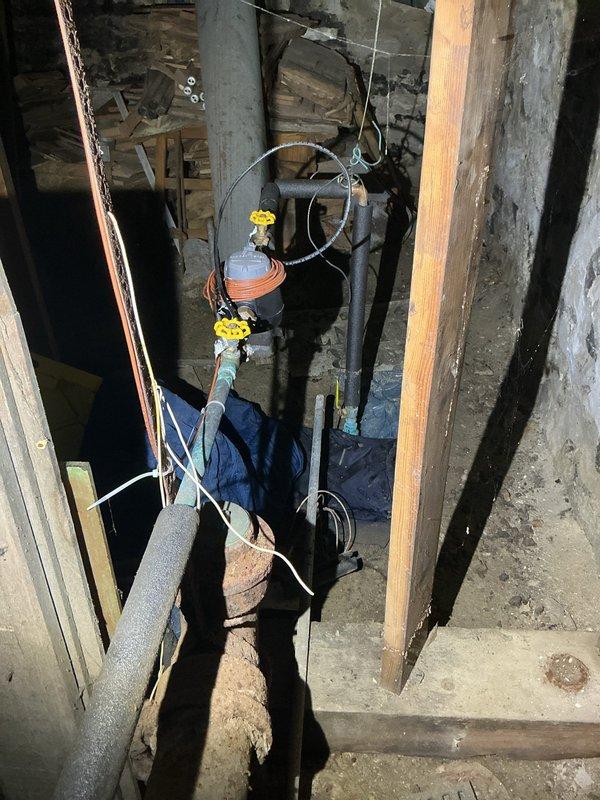 Responded to service call regarding elevated water consumption indicating potential pipe failure. Upon inspection of basement utility area, located and assessed plumbing infrastructure including water supply lines and associated fixtures. Examined exposed piping system with insulated black lines and turquoise-colored tubing, checking for visible leaks, moisture damage, and pressure irregularities. Inspected concrete floor surfaces and surrounding areas for water accumulation, staining patterns, and signs of active leakage that would account for increased water usage. Evaluated condition of pipe connections, valve assemblies, and mechanical joints throughout the accessible crawl space. Documented findings with photographic evidence showing basement plumbing configuration and overall condition of utility infrastructure for service records.