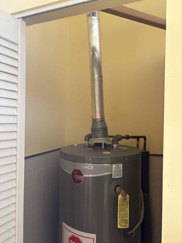 Completed tankless water heater installation estimate and assessment in residential basement utility area. Evaluated existing conditions including traditional Rheem Performance tank-style water heater with vented exhaust system, exposed plumbing infrastructure with white PVC drainage lines, and structural concerns related to water intrusion evident by brown staining on cinderblock walls and moisture damage indicators. Documented current water heater configuration, venting requirements, available space constraints, and necessary modifications for potential tankless conversion including gas line sizing, electrical requirements, and proper combustion air supply considerations.