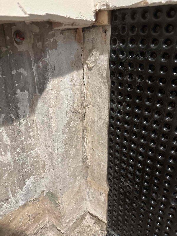 Responded to water leak originating from recently installed drain tile system at foundation level. Upon arrival, discovered active moisture intrusion at the junction where drain tile meets foundation wall, causing water damage to interior basement walls and ceiling materials. Identified compromised waterproofing membrane seal at corner transition point between existing concrete foundation and dimpled drainage membrane. Inspected deteriorated concrete surfaces showing vertical cracking, spalling, and moisture staining, along with visible mold growth on wall surfaces. Assessed damaged ceiling materials and exposed structural elements affected by water infiltration. Documented extensive water damage including discolored drywall, compromised particle board, and deteriorated wall finishes. Collected remaining balance payment for previous drain tile installation work. Photographic documentation captured for insurance and warranty purposes showing foundation corner conditions, membrane instal