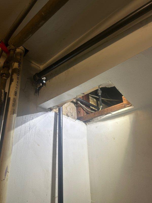 Accessed mechanical chase through wall opening to inspect gas piping system. Located and evaluated black iron gas line configuration with T-junction and shut-off valve in ceiling area near HVAC ductwork. Documented existing gas line routing along ceiling joists, including yellow CSST flexible gas lines with required identification tags. Verified accessibility to gas system components for future service needs. Provided photographic documentation of gas piping infrastructure and structural access point for customer records.