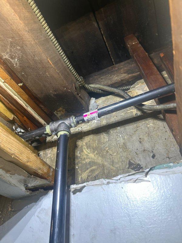 Accessed mechanical chase through wall opening to inspect gas piping system. Located and evaluated black iron gas line configuration with T-junction and shut-off valve in ceiling area near HVAC ductwork. Documented existing gas line routing along ceiling joists, including yellow CSST flexible gas lines with required identification tags. Verified accessibility to gas system components for future service needs. Provided photographic documentation of gas piping infrastructure and structural access point for customer records.