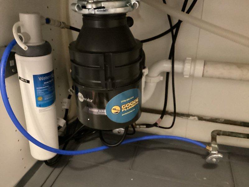 Responded to service call for small leak under kitchen sink. Upon inspection, identified leak originating from garbage disposal unit connections. Examined InSinkErator Edge Series disposal unit, associated PVC drainage piping, and Wellness brand water filtration system. Tightened mounting hardware at sink flange connection and verified all drain line connections for proper seal. Inspected discharge plumbing and confirmed secure attachment of drain pipes to disposal outlet. Tested disposal operation and checked for leaks under running water conditions. All connections secured and leak resolved successfully.