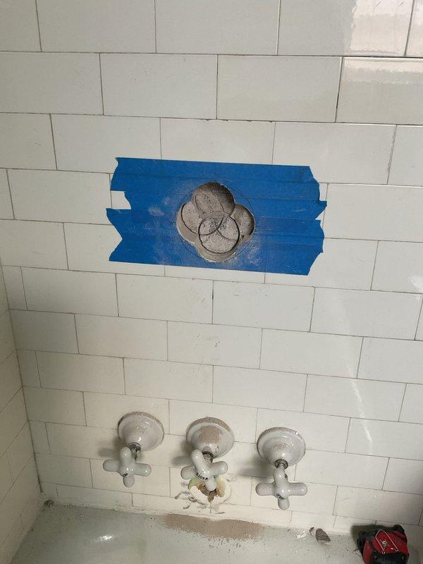 Completed plumbing repair work on a three-handle tub and shower valve system. Addressed water staining and discoloration around the middle valve handle, accessed plumbing fixture behind tile wall using protective masking, and ensured proper operation of all chrome-finished trim components and tub spout.