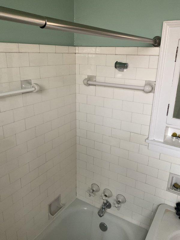 Completed plumbing repair work on a three-handle tub and shower valve system. Addressed water staining and discoloration around the middle valve handle, accessed plumbing fixture behind tile wall using protective masking, and ensured proper operation of all chrome-finished trim components and tub spout.