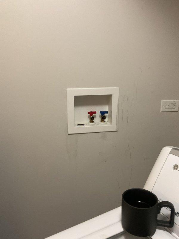 Responded to a priority service call for a leaking cold water shutoff valve at the washing machine connection and a loose toilet flush handle. Inspected the recessed wall box containing the hot and cold water supply valves with color-coded handles and brass fittings. Repaired the leaking cold water shutoff valve and tightened the loose toilet flush handle mechanism to restore proper operation of both fixtures.