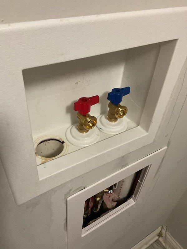 Responded to a priority service call for a leaking cold water shutoff valve at the washing machine connection and a loose toilet flush handle. Inspected the recessed wall box containing the hot and cold water supply valves with color-coded handles and brass fittings. Repaired the leaking cold water shutoff valve and tightened the loose toilet flush handle mechanism to restore proper operation of both fixtures.
