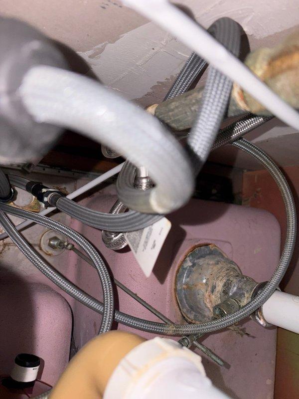 # Plumbing Service - Water Leak Repair

Responded to service call for active water leak beneath kitchen sink in 70-year-old residential property. Upon arrival, confirmed water leaking from supply line connection when faucet was activated. Conducted thorough inspection of under-sink plumbing assembly, identifying failed connection at braided flexible supply line fitting.

Shut off water supply at angle stop valve to prevent further water damage. Removed deteriorated braided stainless steel supply line showing signs of age-related failure at compression fitting. Inspected mounting hardware, valve assembly, and adjacent PVC drain lines for additional wear or damage. Found purple-colored valve component with multiple connections showing normal wear but maintaining structural integrity.

Cleaned and prepared connection points, removing mineral deposits and old thread tape. Installed new braided flexible supply line with proper brass compression fittings. Tightened all connections to manufac