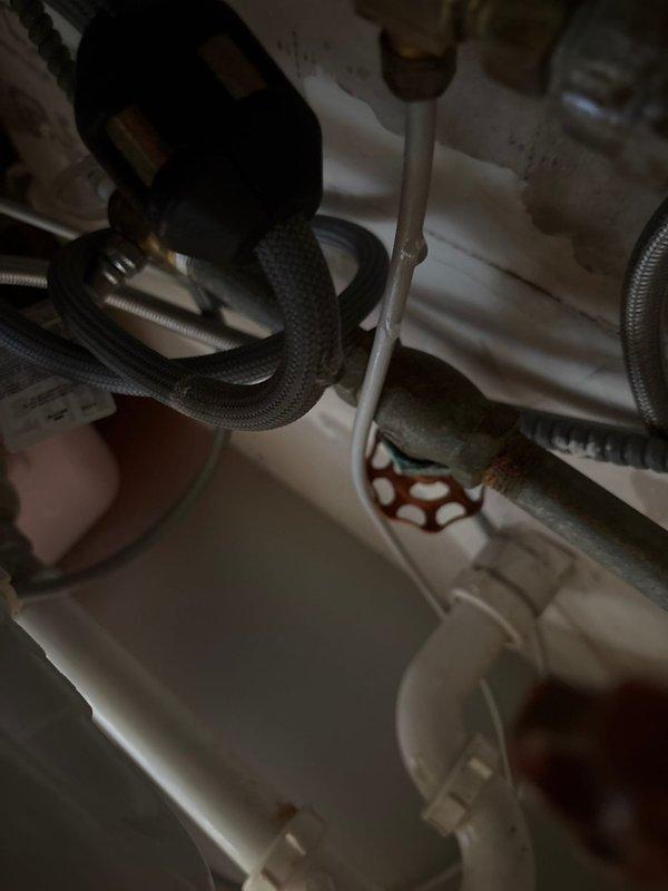 # Plumbing Service - Water Leak Repair

Responded to service call for active water leak beneath kitchen sink in 70-year-old residential property. Upon arrival, confirmed water leaking from supply line connection when faucet was activated. Conducted thorough inspection of under-sink plumbing assembly, identifying failed connection at braided flexible supply line fitting.

Shut off water supply at angle stop valve to prevent further water damage. Removed deteriorated braided stainless steel supply line showing signs of age-related failure at compression fitting. Inspected mounting hardware, valve assembly, and adjacent PVC drain lines for additional wear or damage. Found purple-colored valve component with multiple connections showing normal wear but maintaining structural integrity.

Cleaned and prepared connection points, removing mineral deposits and old thread tape. Installed new braided flexible supply line with proper brass compression fittings. Tightened all connections to manufac
