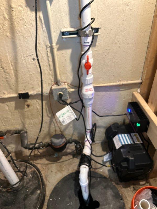 Technician responded to a residential property to complete a sold plumbing repair involving sump pump system installation and drainage configuration. Upon arrival, installed a new sump pump unit in the basement utility area with proper electrical connections, confirmed by illuminated operational indicator lights on the pump housing. Assembled and installed vertical PVC drainage piping with multiple fittings and joints, applying purple primer and securing connections with a red ball valve for system shutoff capability. Coordinated installation with existing radon mitigation system components mounted on the wall to ensure proper clearances and functionality. Verified pump operation, checked for proper water discharge through the newly installed PVC pipe assembly, and confirmed all electrical connections were secure and functioning correctly. System tested and left in operational condition.
