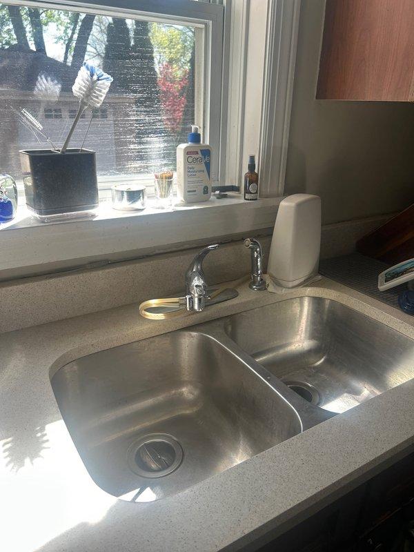 Completed installation of chrome single-handle kitchen faucet on double-basin stainless steel sink with light gray speckled countertop. Verified proper connection to existing plumbing infrastructure including P-trap assembly and garbage disposal unit, confirmed no leaks at all connection points, and tested full water flow and temperature control functionality.