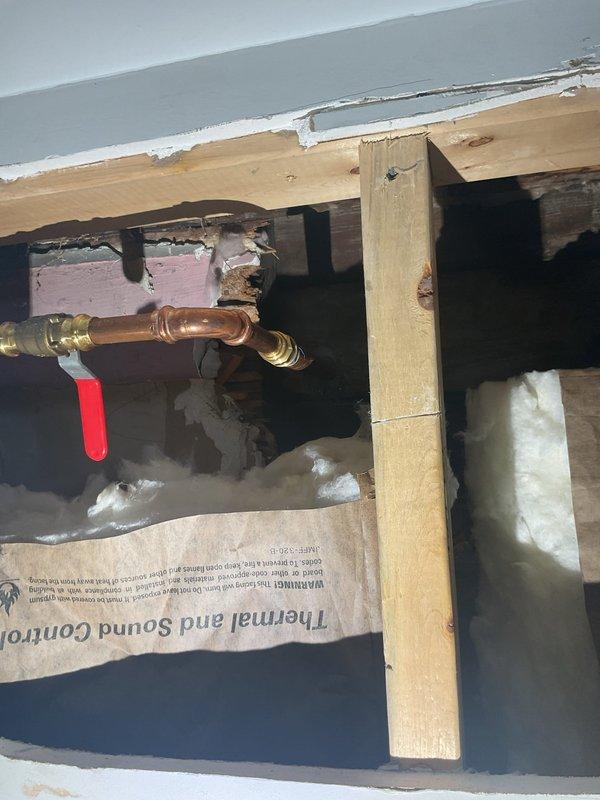 Responded to outdoor hose line leak in 121-year-old home where water supply had been shut off since January. Accessed plumbing system through crawl space/floor joist area and identified severely corroded copper pipe with compromised brass compression fittings as source of leak. Replaced deteriorated section of copper supply line and installed new brass shut-off valve with red handle. Secured new piping properly within existing floor joist cavity and verified all connections were leak-free before restoring water supply to outdoor spigot system.