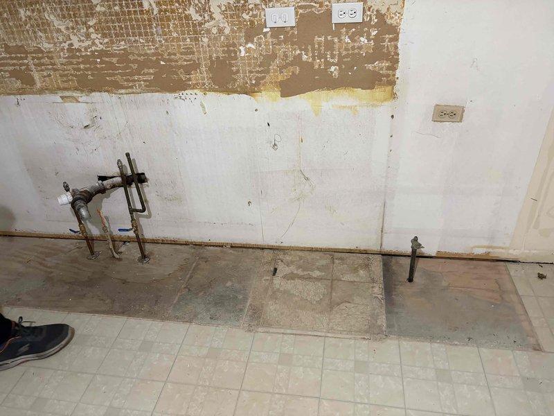 Conducted plumbing estimate for kitchen piping replacement in 60-year-old residential property. Assessed multiple exposed metal pipes protruding from deteriorated wall surfaces, noting corrosion and aging of existing plumbing fixtures. Documented condition of obsolete piping system requiring replacement due to age-related deterioration consistent with original home construction.
