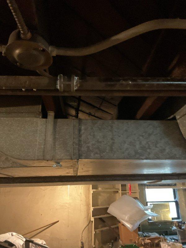 Conducted comprehensive assessment of gas piping system in 125-year-old residential basement requiring replacement. Inspected existing galvanized gas lines running through exposed ceiling joists alongside electrical wiring and HVAC ductwork. Evaluated routing and condition of gas supply lines servicing water heater and furnace equipment. Documented current piping configuration, including connections to green cylindrical water heater tank and beige furnace unit with associated PVC venting. Assessed accessibility for replacement work given proximity to stored items and existing mechanical systems. Provided estimate for complete gas line replacement to ensure safe, code-compliant installation appropriate for aged residential structure.