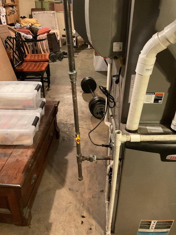 Conducted comprehensive assessment of gas piping system in 125-year-old residential basement requiring replacement. Inspected existing galvanized gas lines running through exposed ceiling joists alongside electrical wiring and HVAC ductwork. Evaluated routing and condition of gas supply lines servicing water heater and furnace equipment. Documented current piping configuration, including connections to green cylindrical water heater tank and beige furnace unit with associated PVC venting. Assessed accessibility for replacement work given proximity to stored items and existing mechanical systems. Provided estimate for complete gas line replacement to ensure safe, code-compliant installation appropriate for aged residential structure.