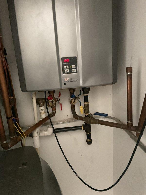 Responded to no hot water emergency at residential property. Upon arrival, assessed basement water heating system and determined existing tanked water heater had failed. Removed and replaced failed conventional tank-style water heater with new tankless water heating unit. Installed tankless system on basement wall with proper mounting and clearances. Connected copper supply lines with shut-off valves featuring color-coded hot and cold water controls. Integrated white PVC piping for venting and drainage requirements. Installed electrical connections and verified proper power supply to unit. Tested all plumbing connections for leaks, confirmed proper water flow, and programmed digital control panel. Verified system operation and restored hot water service to residence. Installation completed with all connections secure and unit functioning within manufacturer specifications.