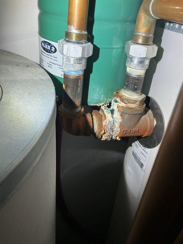 Responded to report of sewer gas smell and performed smoke test to identify source of odor intrusion. Investigation revealed compromised wall penetration in utility area near water heater installation, with visible deterioration of drywall and interior materials allowing sewer gases to enter living space. Documented existing mineral buildup on water heater connections and exposed wall opening requiring proper sealing to prevent further gas migration into the structure.