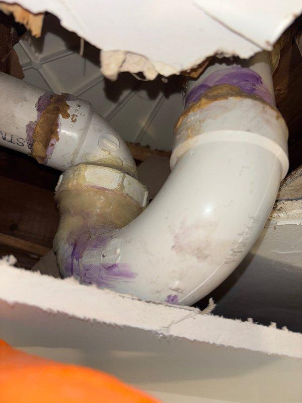 Completed plumbing repair involving PVC drain line installation in ceiling cavity above bathroom. Replaced damaged drainage piping with new white PVC elbows and connectors, applied proper purple primer and solvent cement to all joints per code requirements. Protected bathroom floor with drop cloths during overhead work, maintained clean work area throughout service call.