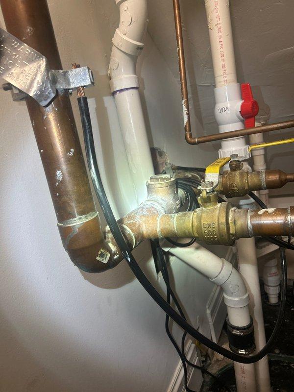 Responded to callback for multiple plumbing issues on combi boiler system. Inspected existing piping configuration including copper supply lines, PVC drainage, and brass valve assembly showing signs of age and mineral deposits. Evaluated condensate trap for potential replacement due to visible corrosion and buildup on metal fittings beneath unit. Assessed building valve and identified active leak requiring attention. Provided estimate options for full combi boiler replacement versus condensate trap replacement and unit shutoff valve installation to address immediate concerns and improve system serviceability.