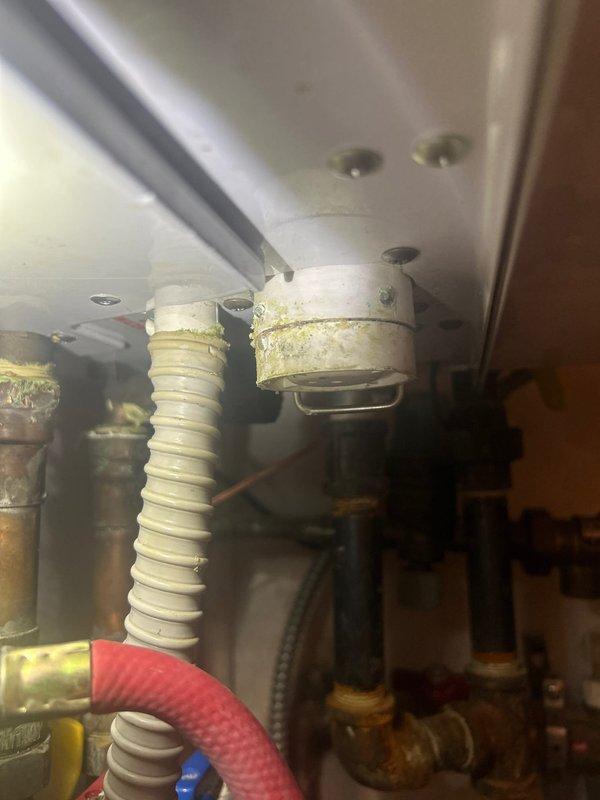 Responded to callback for multiple plumbing issues on combi boiler system. Inspected existing piping configuration including copper supply lines, PVC drainage, and brass valve assembly showing signs of age and mineral deposits. Evaluated condensate trap for potential replacement due to visible corrosion and buildup on metal fittings beneath unit. Assessed building valve and identified active leak requiring attention. Provided estimate options for full combi boiler replacement versus condensate trap replacement and unit shutoff valve installation to address immediate concerns and improve system serviceability.