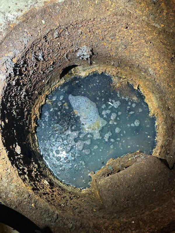 Responded to service call for catch basin cleaning in basement utility area. Upon arrival, located catch basin in corner of basement with visible deterioration and corrosion throughout interior pipe walls. Basin contained standing water with debris accumulation and sediment buildup along edges. Performed thorough cleaning of catch basin, removing debris, sediment, and buildup from interior surfaces. Documented pre-service and post-service conditions with photographs showing extent of corrosion and water accumulation. Basin restored to proper drainage function.