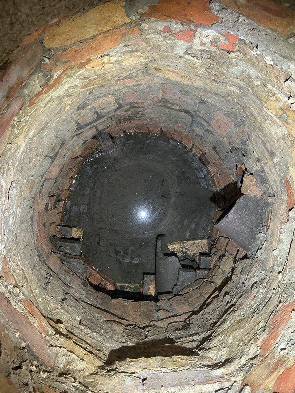 Conducted inspection of sump pump system accessed through utility room floor opening. Removed access panel to evaluate brick-lined sump pit condition and pump operation. Documentation revealed significant deterioration of brick and mortar within the vertical shaft, with visible structural degradation, crumbling mortar joints, and moisture damage throughout. Observed debris accumulation at pit bottom and evidence of previous repair attempts. Photographed existing conditions for service records. Follow-up appointment scheduled to complete necessary repairs and system restoration.