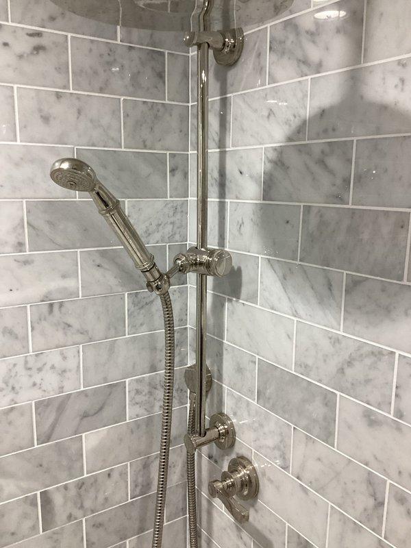 Conducted follow-up site visit to assess shower valve system requiring replacement parts. Inspected chrome shower fixture assembly mounted on marble-patterned tile surround, including pressure-balance valve control, handheld showerhead with flexible hose, and sliding bar system. Documented installation configuration and verified part specifications needed for ordering, with photos taken for reference to ensure correct component procurement for upcoming repair completion.